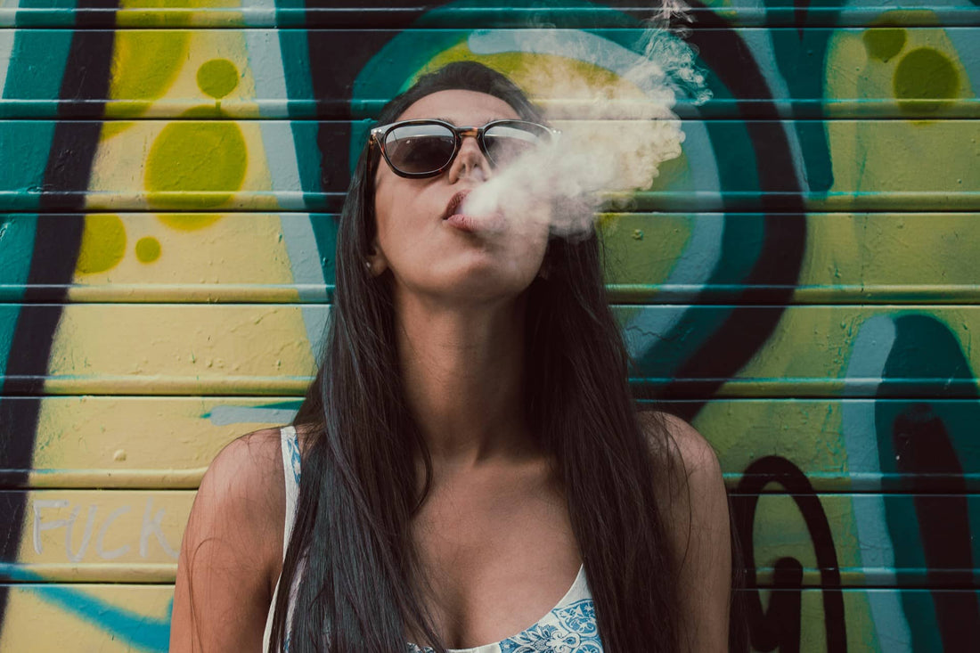 woman in sunglasses smoking against graffiti background